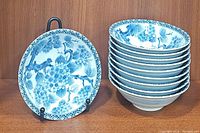 Stack of nine and one displayed blue and white cherry blossom patterned Japanese soup bowls with geometric border.
