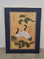 Full view of framed canvas artwork showing two red crowned cranes on pine branches with navy blue and gold border.