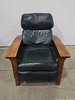 Front view of the black leather mission style recliner chair showing padded seat, backrest, and wooden armrests.