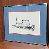 Full view of the framed tugboat artwork matted in blue with a red border and a wooden frame.