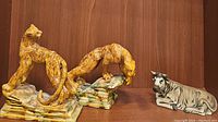 Two Royal Haeger ceramic leopard bookends in yellowish brown glaze and a separate beige and brown resting bull figurine on wood shelf.