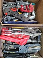 Two boxes, one filled with assorted pliers and hand tools showing a variety of metal tools primarily with red handles; includes locking pliers and a staple gun