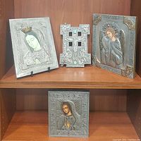 Four religious metal relief plaques including Saint Michael, two Mother Mary plaques, and a small crucifix displayed on wooden shelving.
