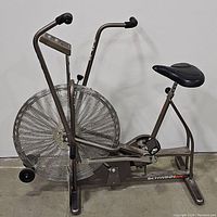 Front-left view showing large fan wheel, dual-action handlebars, seat and pedal assembly