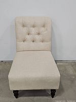 Front view showing the cream colored tufted backrest and cushioned seat of the slipper chair.