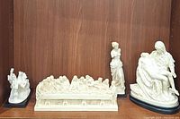 Four statues on a shelf: Pieta on oval black base, The Last Supper relief, goddess standing figure and chariot with horses.