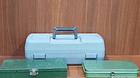 Closed green metal socket wrench set case and smaller green metal ratchet set case next to blue Dremel case.