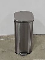 Metal trashcan with foot pedal lid closed, showing clean brushed stainless steel body.