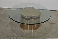 Overall front view of the round glass top coffee table with brass trefoil base showing shape and materials.