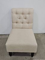 Front view of cream colored tufted slipper chair showing button tufted backrest, cushioned seat, and front wooden legs.