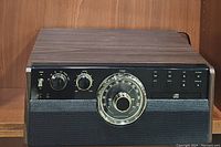 Front view of the Victrola Empire VTA-370B showing wood finish and analog radio dial with control knobs.