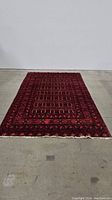 Full view of vintage geometric knotted area rug laid flat on floor, maroon-red dominant color with fringed edge.