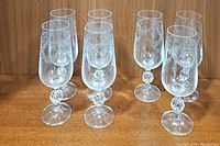Seven vintage etched champagne flutes in two rows on wooden surface, front view