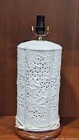 Full view of the white porcelain lamp showing the reticulated design, raised figure and cord wrapped around base.