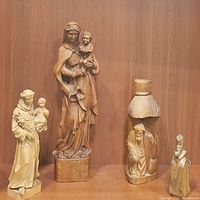 Lot of four vintage hand-carved wooden religious figurines on a wood background; includes Madonna and child, Saint Anthony with child, kneeling man, and priest figure.