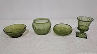 Four green glass vintage items: textured avocado green glass bowl, ridged humidor, swirl pattern bowl, and footed scalloped vase/candle holder.