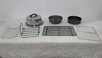 Full set image showing metal cake plate and dome, Bundt pan, round cake pan, and four baking racks arranged on white cloth.