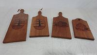 Four wooden cutting boards laid out side by side showing etched designs and hanging features.
