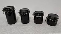 Front angle showing four black canisters of varying heights with clamp metal lids.
