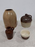 Set of four brown pottery and stoneware items including a large vase, a jug, a pitcher and a small bowl laid out on a white cloth background.