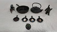 Wide angle view of all cast iron items including Amish Horse and Buggy figurine, skillet, teapot, Scottie dog figurine, four mini cast iron painted pans, and small cast iron wall plaque