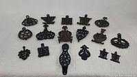 Overview photo of all 17 cast iron trivets arranged on a white surface showing diverse decorative designs and sizes.