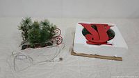 Two holiday decorations: a Christmas sled with artificial greenery and pinecones, and a Joy wreath with candle holders, placed on a quilted surface.