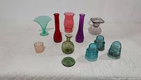 Grouped photo of assorted colored glass items including various vases, insulators, votive holder and coaster arranged on white cloth