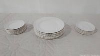 Three stacks of plates showing large, medium, and small sizes arranged from center to sides on a quilted white surface.