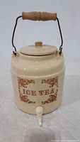 Full view of vintage stoneware ice tea crock with wooden handle, lid, and spigot, showing front reading 'ICE TEA'.