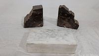 Photo showing two brown marble bookends placed behind a white marble rectangular block on a white cloth background.