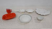 Full view of vintage kitchenware mix including orange milk pitcher, white baking dishes, clear glass bowl, and lotus-shaped bowl.