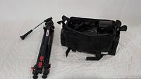 Photo showing SkyHawk tripod and black camera bag containing accessories on a white surface.
