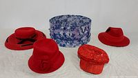 All four red hats and the large blue floral patterned hat box arranged on white surface