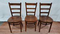 Front view of three Thonet bent wood chairs showing shape, wood finish, and ladder-style backs.