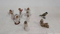 Six Willow Tree angel figures, Chac Mool resin statue, and wooden bird displayed together on white surface.