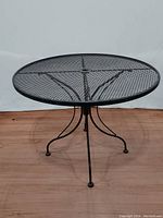 Front side photo of the round wrought iron table showing the mesh top and four legs with curved design.