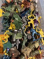 Top-down photo showing a pile of assorted yellow and green plastic army figurines and one visible green plastic toy vehicle.