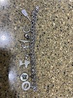 Full view of the silver charm bracelet with all seven charms laid out on a stone countertop.