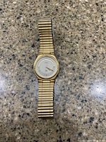 Full view of the gold-tone men's Seiko wristwatch lying flat on granite surface showing its face and metal stretch band.