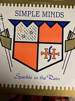 Close-up front cover of the vinyl record album Sparkle in the Rain by Simple Minds showing stylized crest artwork and text.