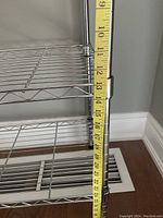 Metal shelving rack close up showing the vertical support pole with shelf height adjustment detail and tape measure indicating shelf heights.