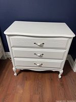 Front view of white 3-drawer dresser showing decorative carving and curved legs