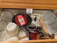 Drawer containing various baking tools such as pans, rolling pin, cooling rack, cookie cutters, plastic citrus juicer, and hand mixer parts.