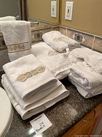 Photo of stacked white bathroom towels with beige and gold embroidery on countertop.