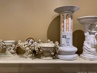 Wide view of 5 cherub-themed candle holders lined up on a shelf.