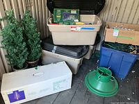 View of boxed artificial trees, storage bins with loose and boxed lights, and green tree stand on floor of shed.