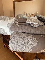 Queen size reversible comforter laid out showing brown side with floral pattern, layered with folded quilted coverlet and pillowcases on top.