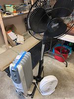 Photo showing all three items: black pedestal fan, white box fan, white oil heater on wheels.