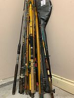 Photo showing a collection of fishing rods stored together, leaning against a wall.